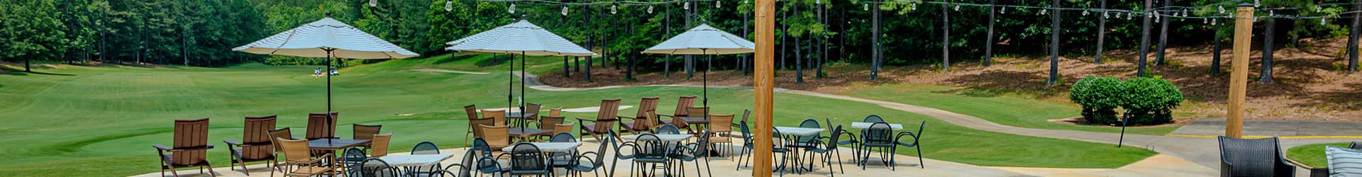 A tranquil outdoor lounge area with tables and chairs under umbrellas, surrounded by greenery and decorative lights.
