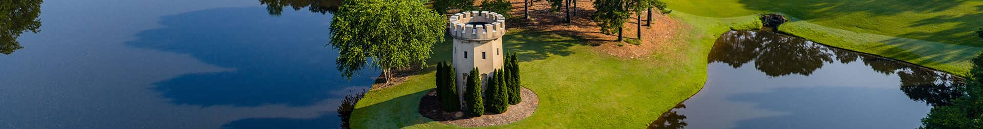 Aerial view of a charming stone tower surrounded by lush greenery and serene water, reflecting nature's beauty.