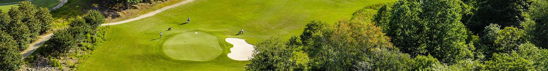 A beautiful panoramic view of a green golf course featuring a sand trap and putting green with golfers in the distance.