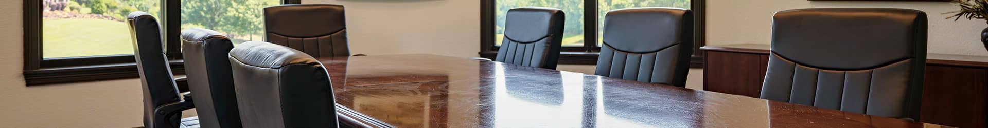 A bright meeting room featuring a polished wooden conference table with ergonomic chairs and large windows.